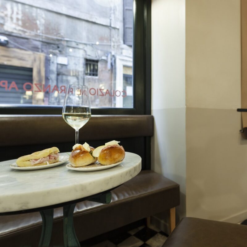 tavolino rotondo con calice di vino bianco e panini farciti