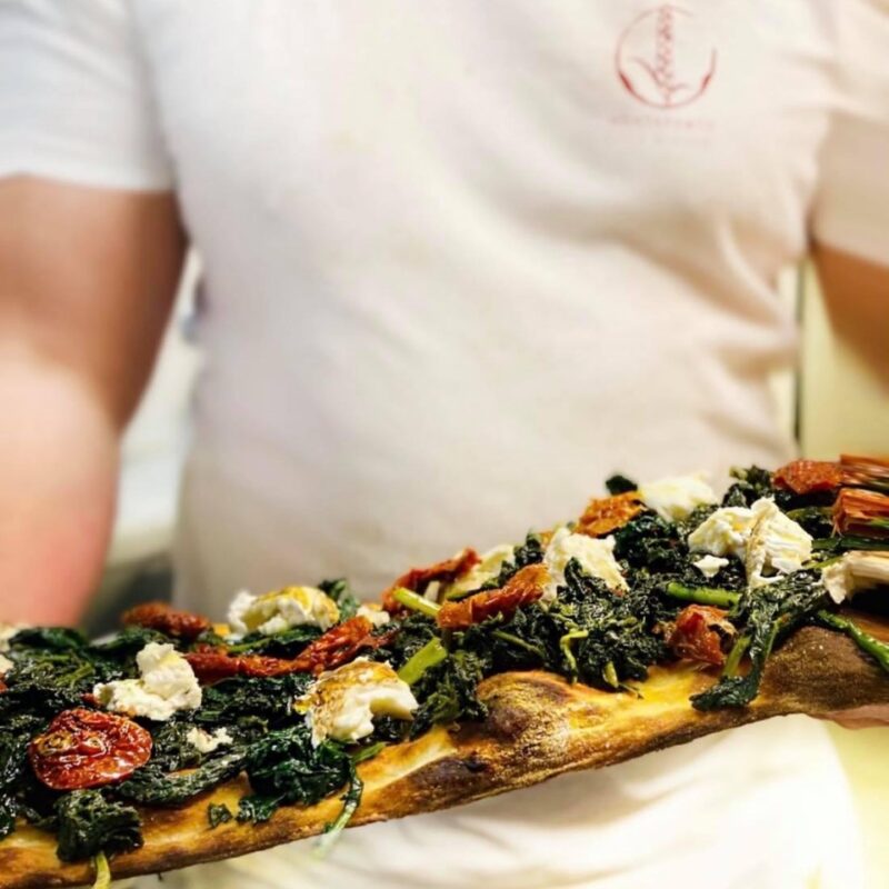 pizzaiolo con pizza alla pala con verdura, formaggio e pomodori secchi